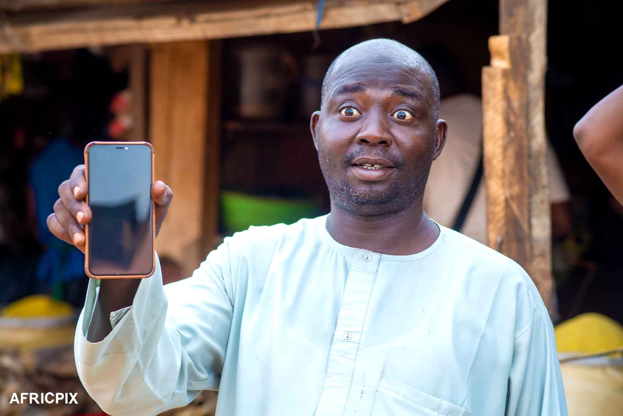 Nigeria Market Man In Front of Shop Holding A Phone Looking Surprise